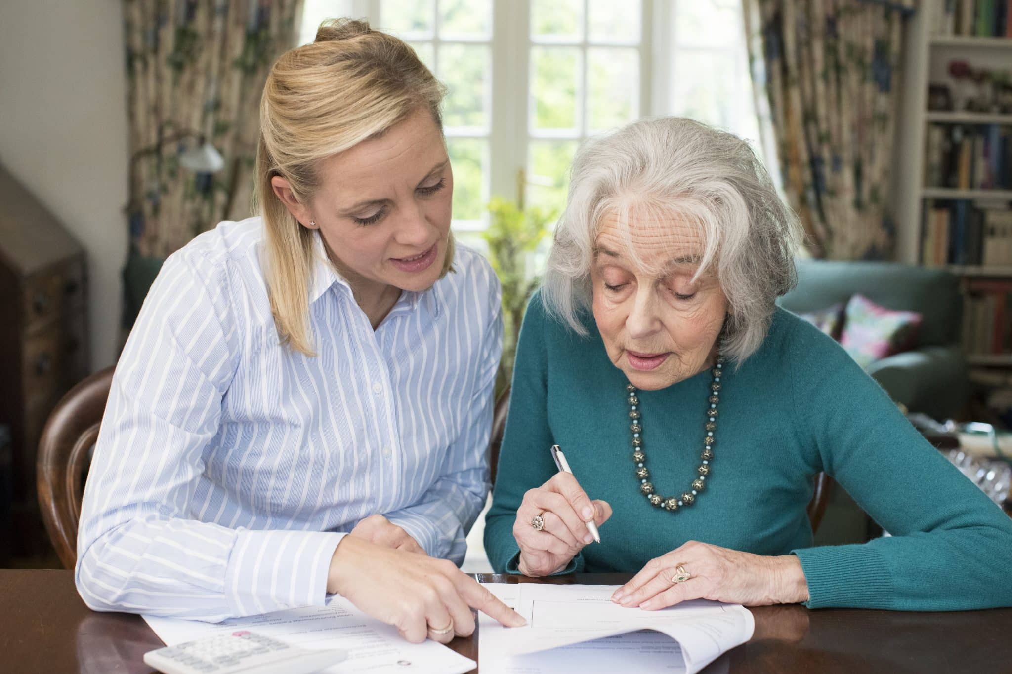 Woman Helping Senior Neighbor With Paperwork First At Home